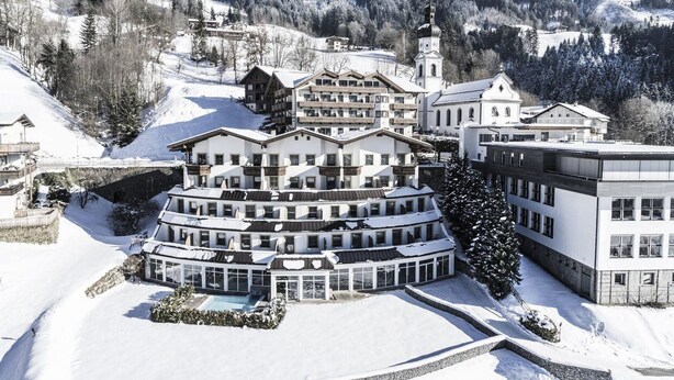 A multi-story hotel with a central courtyard and a pool, surrounded by snow-covered hills and trees. - Ferienhotel Hoppet (Hart im Zillertal)