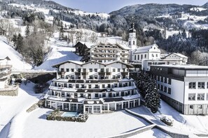 A multi-story hotel with a central courtyard and a pool, surrounded by snow-covered hills and trees. - Ferienhotel Hoppet (Hart im Zillertal)