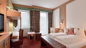A hotel room with a bunk bed, a desk with a chair, a small table with a vase, and a bedside table with a lamp. - Ferienhotel Hoppet (Hart im Zillertal)