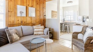 Una sala de estar acogedora con techo de madera, un sofá, una mesita redonda y un sillón de mimbre.