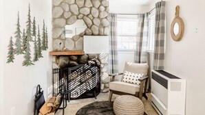 Un rincón acogedor con chimenea de piedra, una silla, una mesita y un radiador.