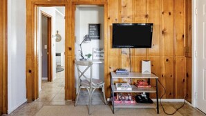 Habitación con paneles de madera, un televisor de pantalla plana en la pared, un escritorio con una silla y una estantería con libros y una lámpara.