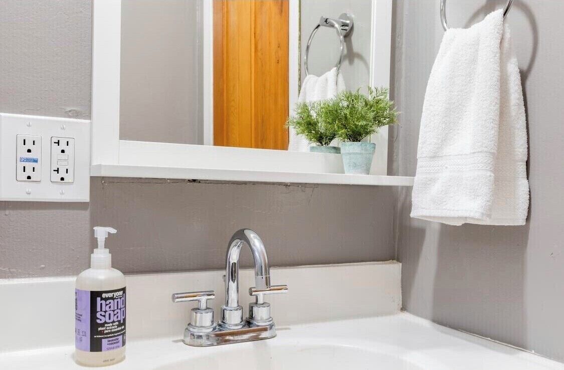A bathroom with a white sink, a mirror, a towel rack, and a potted plant.