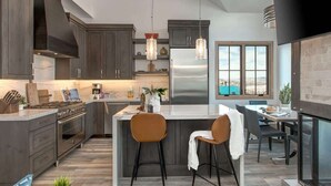 A modern kitchen with dark cabinets, a stainless steel refrigerator, and a large island with bar stools. - Abode at King's Crown, ski-in/ski-out, private hot tub, on private trail (Park City)