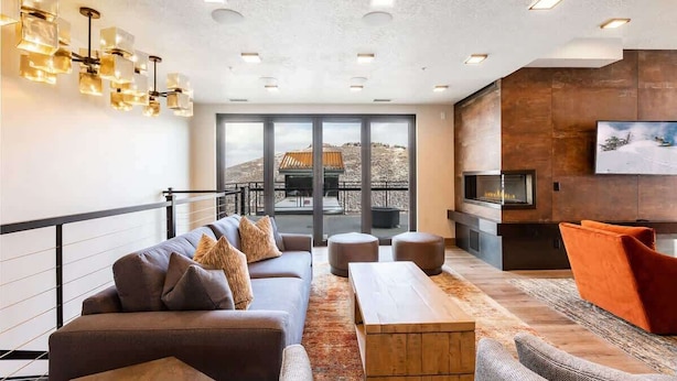 A modern living room with a sofa, ottomans, a coffee table, a fireplace, and a large window with a view. - Abode at King's Crown, ski-in/ski-out, private hot tub, on private trail (Park City)