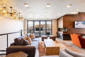 Uma sala de estar moderna com sofá, pufes, mesa de centro, lareira e uma grande janela com vista.
