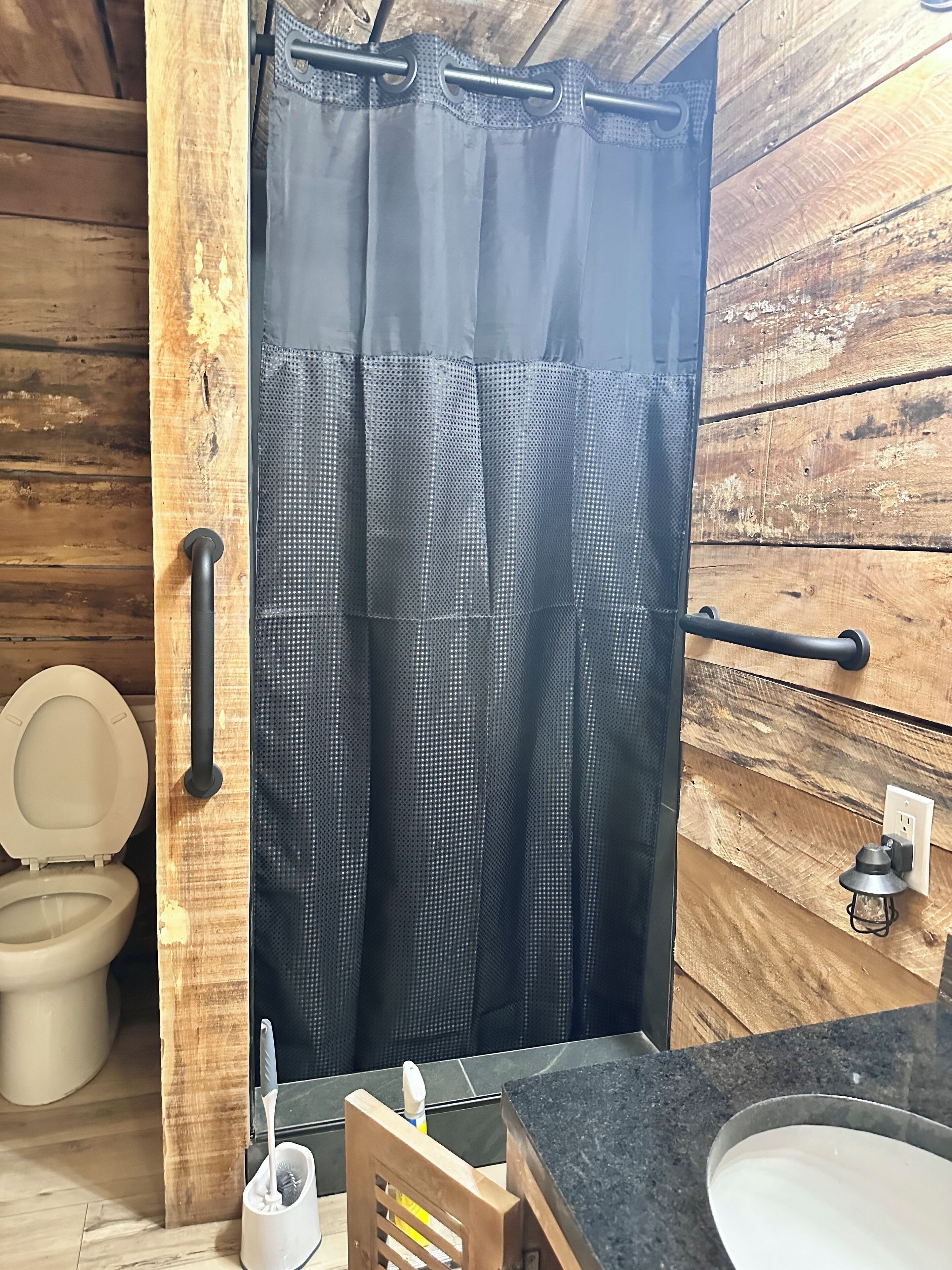 A bathroom with a wooden wall, a toilet, a sink, and a shower curtain.