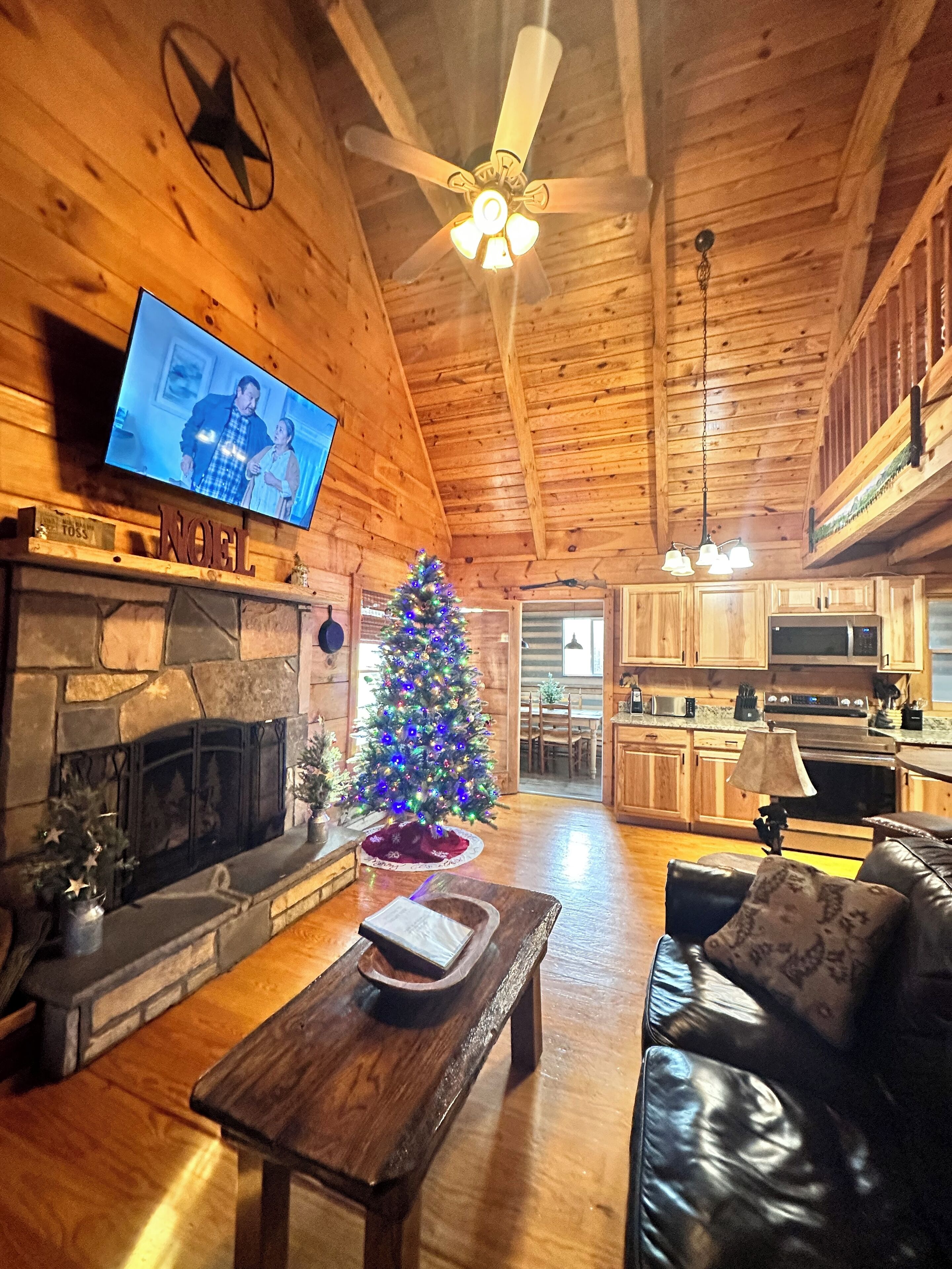 Un intérieur de chalet chaleureux avec une cheminée en pierre, un sapin de Noël, un téléviseur et un coin repas.