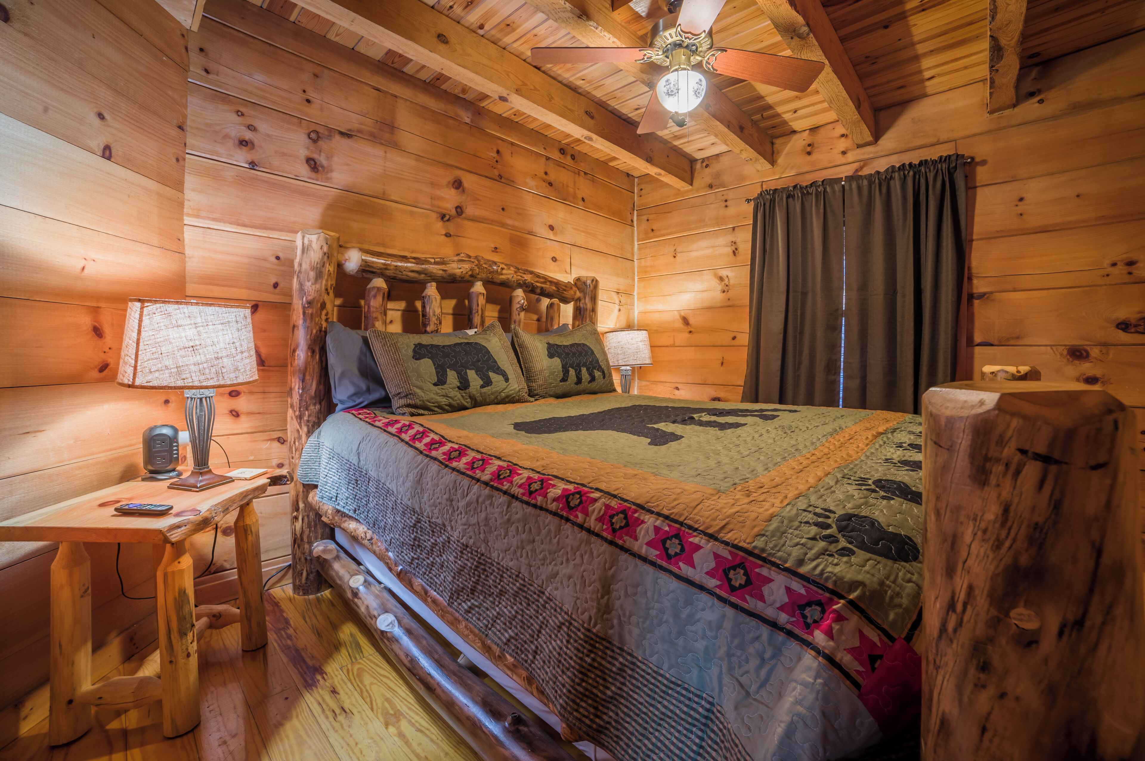 Ein Schlafzimmer einer Holzhütte mit einem Bett, einem Nachttisch, einer Lampe und einem Deckenventilator.