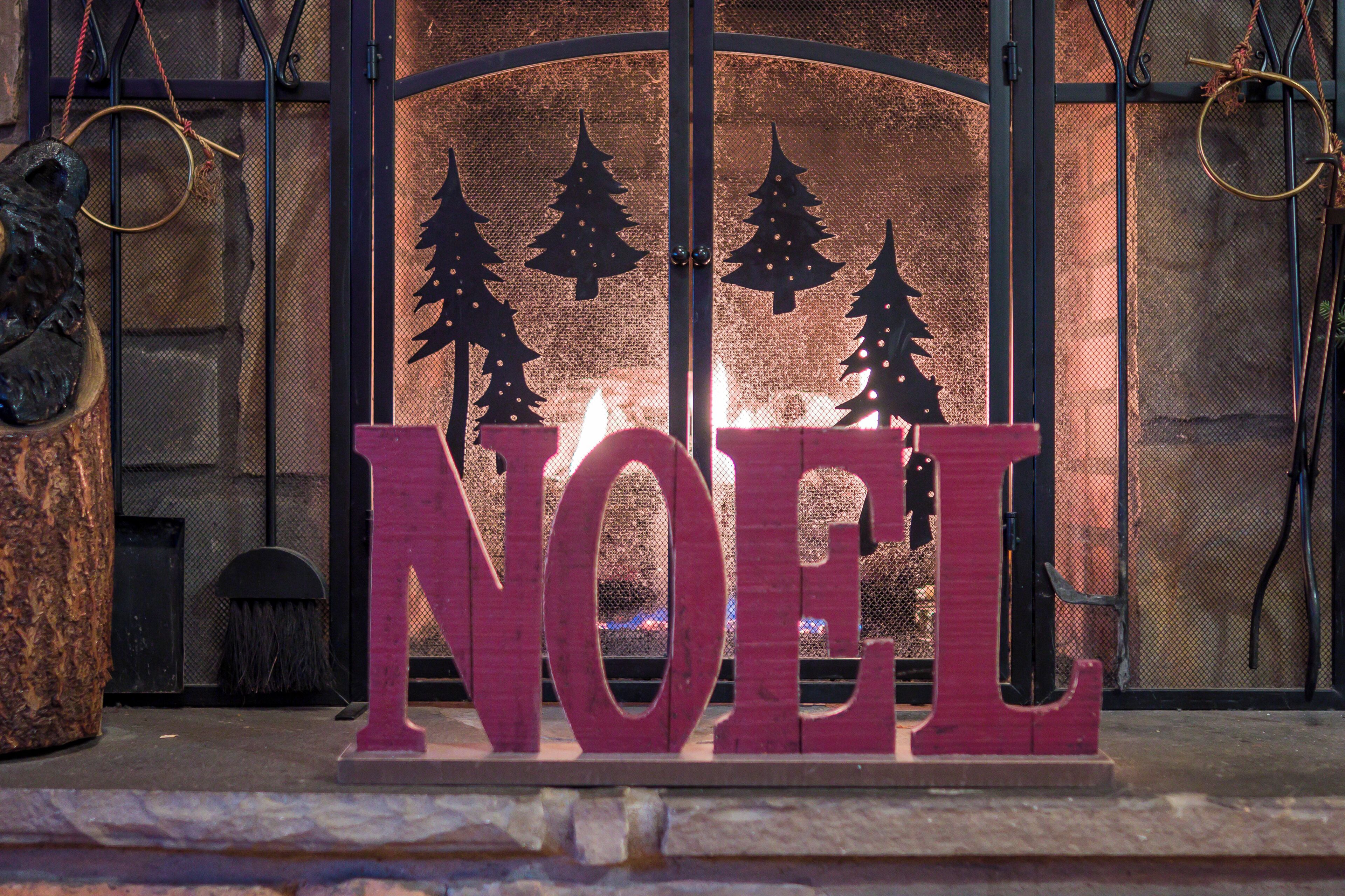 A fireplace with a 'NOEL' sign and Christmas tree silhouettes.