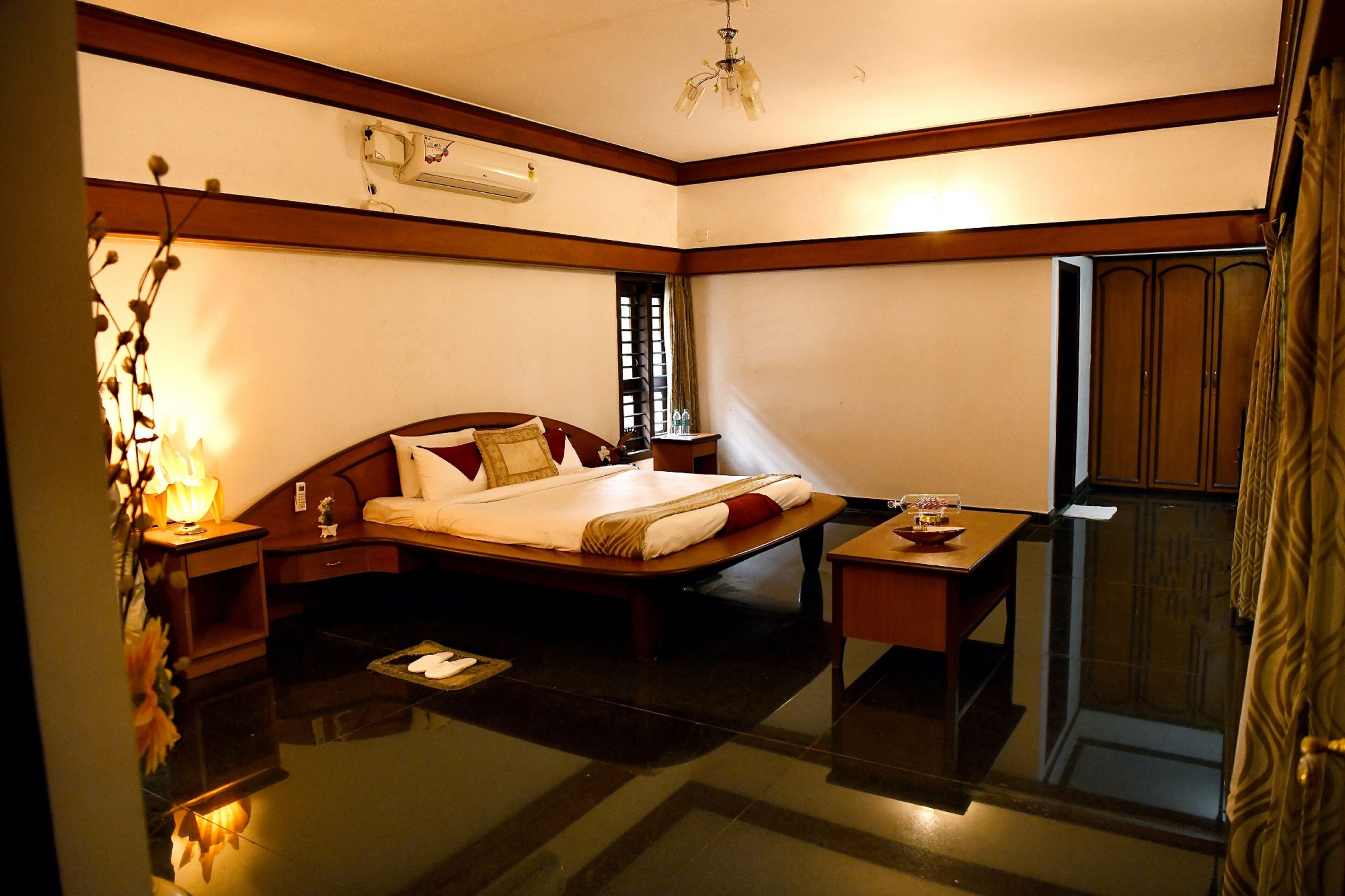 Quarto de hotel com cama, mesa de cabeceira, luminária e espelho.