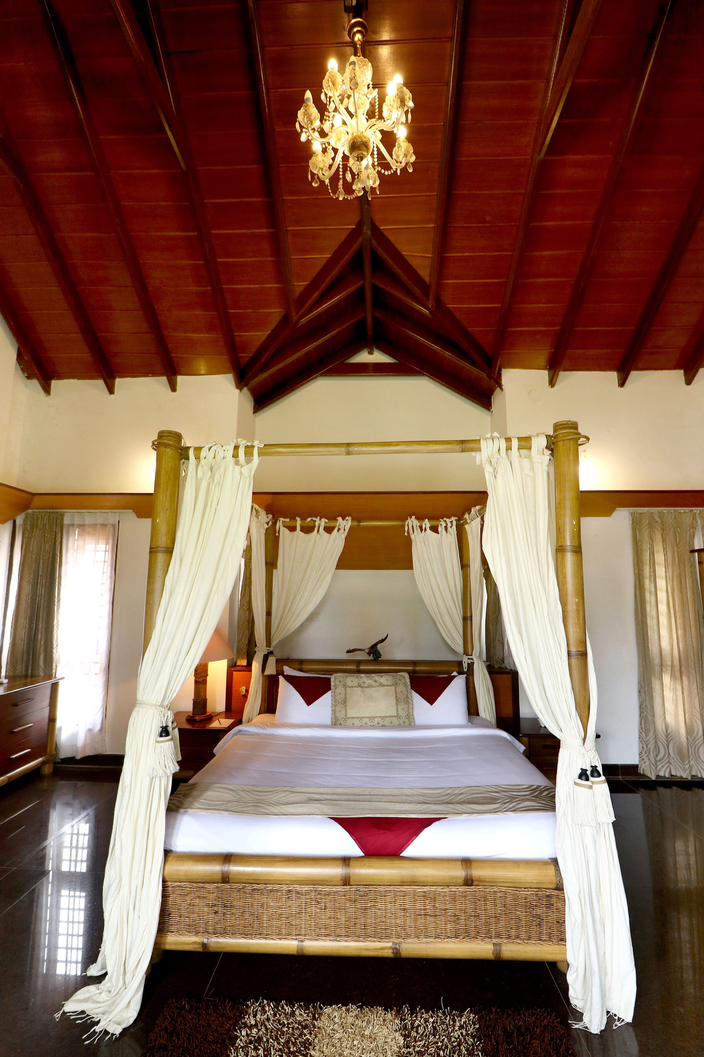 A four-poster bed with white drapes, a chandelier, and a wooden ceiling.