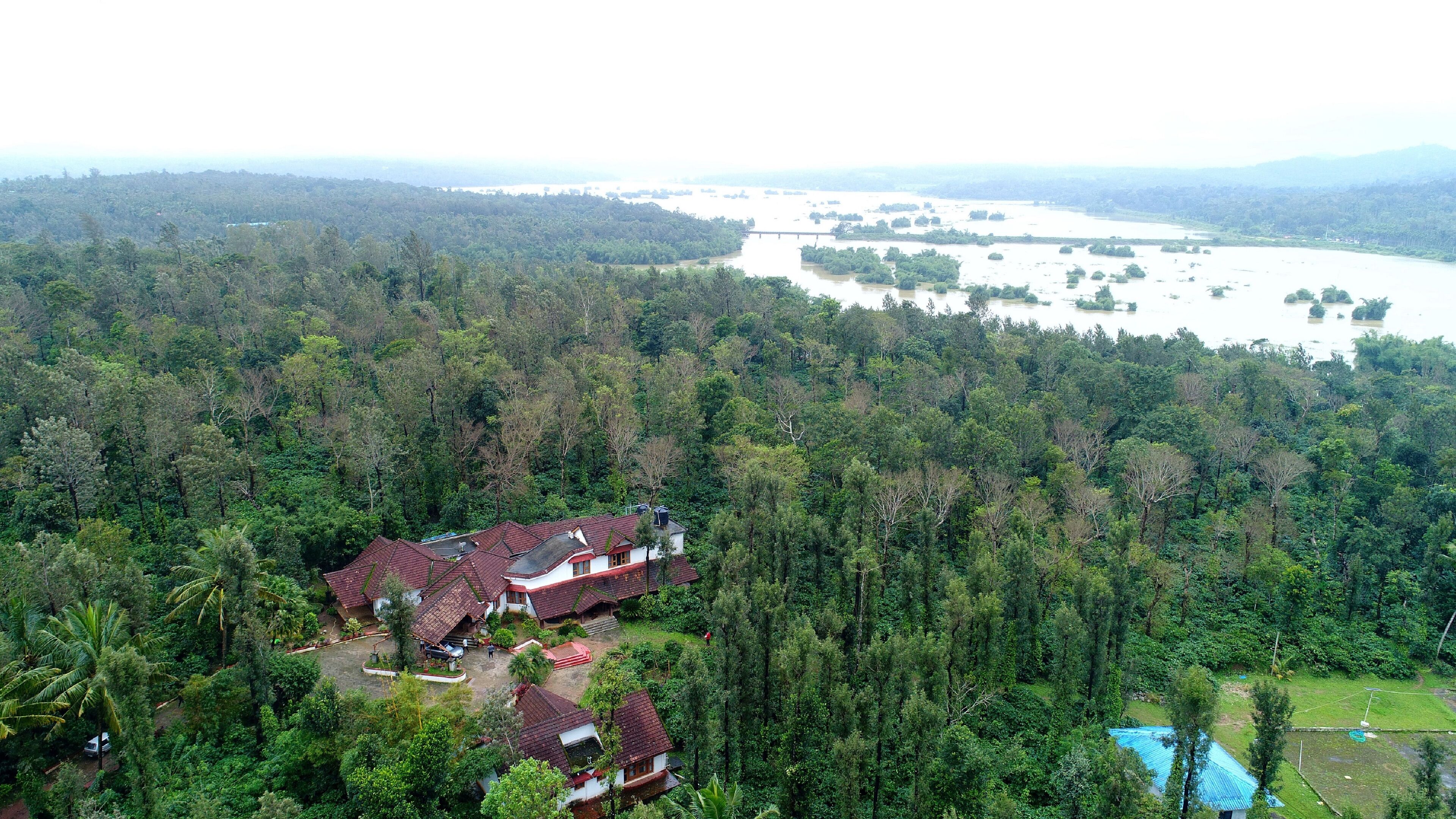 A large, multi-story building with a red roof, surrounded by dense forest and a river in the background.