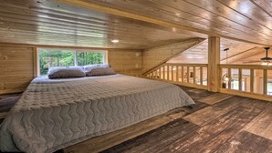 A wooden cabin bedroom with a bed, a window, and a balcony. - Quaint Mtn Cabin: Tiny Living Near Big Adventure (Brevard)