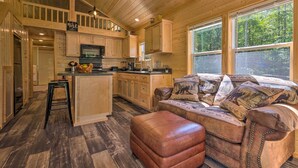 A wooden cabin interior with a kitchen, dining area, and a large window overlooking a forest. - Quaint Mtn Cabin: Tiny Living Near Big Adventure (Brevard)