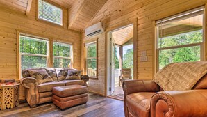 A wooden cabin interior with a leather sofa, ottoman, and a dining table. - Quaint Mtn Cabin: Tiny Living Near Big Adventure (Brevard)