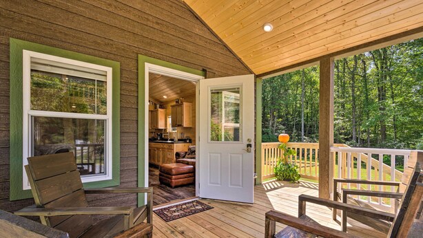A wooden deck with outdoor seating, a door leading to a kitchen, and a view of a forested area. - Quaint Mtn Cabin: Tiny Living Near Big Adventure (Brevard)