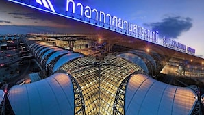 Una moderna terminal de aeropuerto con un letrero iluminado destacado, amplias zonas de espera cubiertas y una estructura de puente.