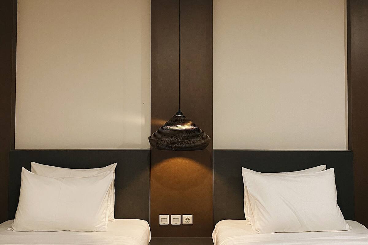 A hotel room with two beds, a central light fixture, and a wall-mounted control panel.