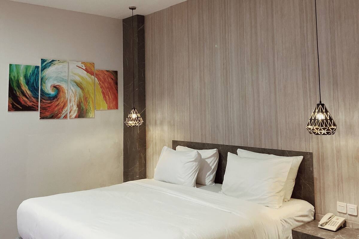 A modern bedroom with a large bed, a wooden headboard, a bedside table with a phone, and two pendant lights.