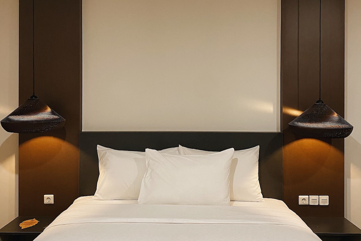 A hotel room with a large bed, two bedside lamps, and a wall-mounted control panel.