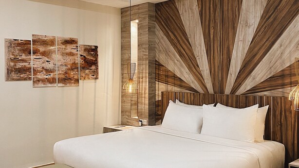 A modern bedroom with a large bed, a wooden accent wall, and a small side table. - Paradise by CaLia Tarakan (Tarakan)