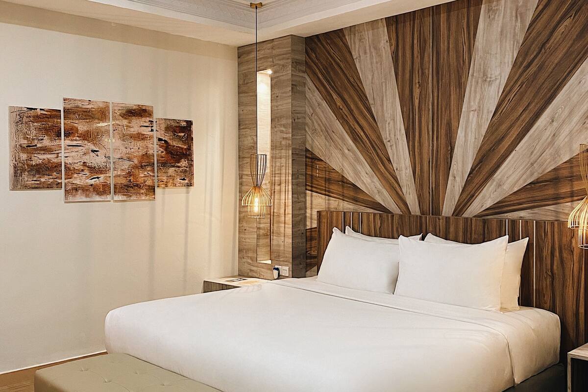 A modern bedroom with a large bed, a wooden accent wall, and a small side table.