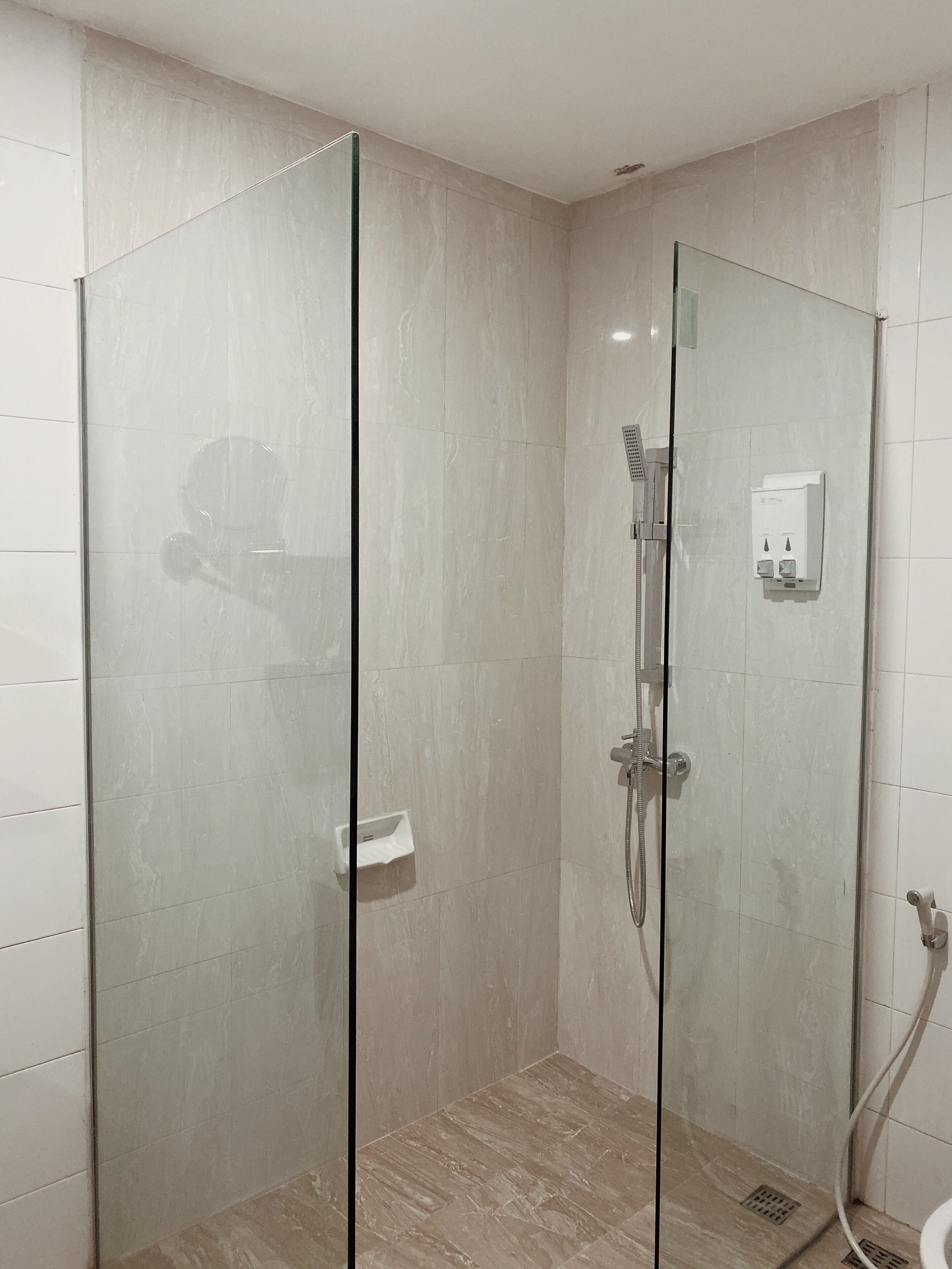 A glass-enclosed shower stall with a handheld showerhead and a wall-mounted control panel.