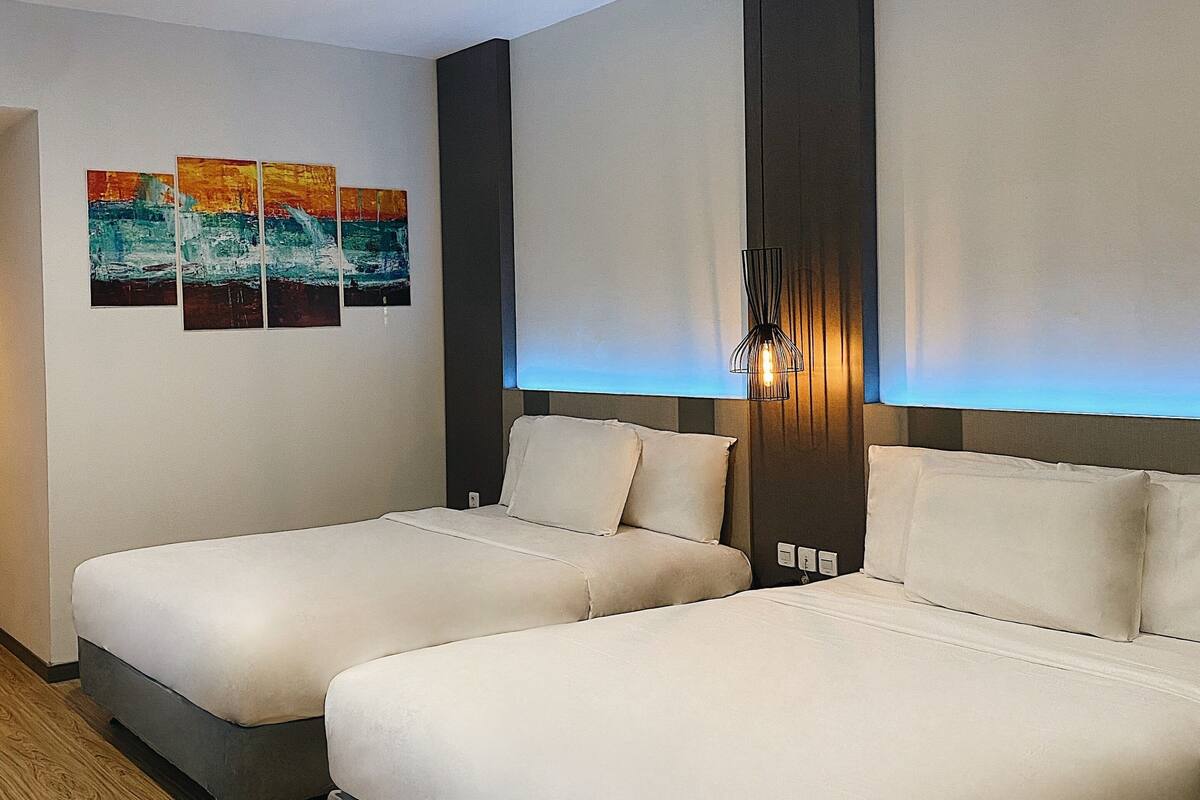 A hotel room with two beds, a wooden floor, and a wall with three colorful paintings.