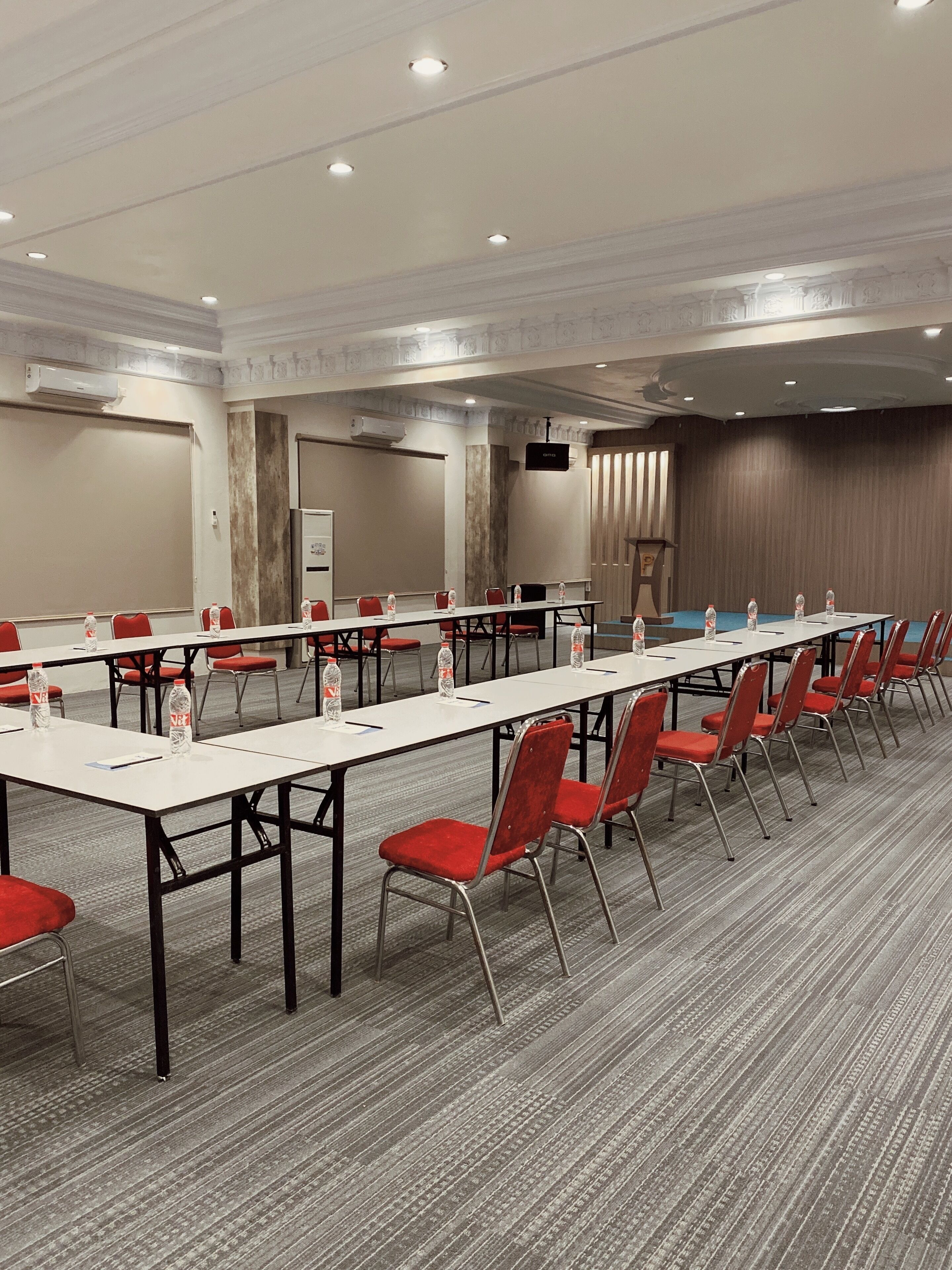 A conference room with long tables, red chairs, water bottles, and a projector screen.