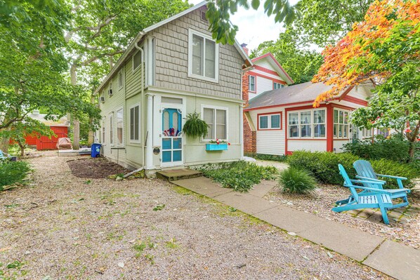 A two-story house with a front porch, a blue Adirondack chair, and a hanging plant.