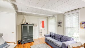 A living room with a grey sofa, a wooden rocking chair, a fireplace, and a window with blinds. - Walk to Lake: Historic Lakeside Marblehead Cottage (Lakeside Marblehead)