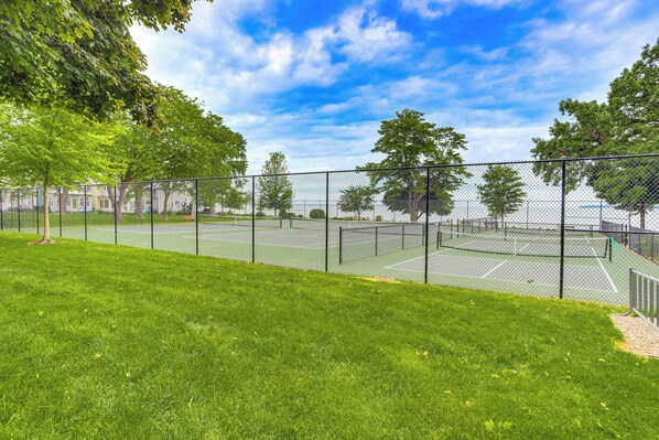 A tennis court with a chain-link fence, surrounded by green grass and trees. - Walk to Lake: Historic Lakeside Marblehead Cottage (Lakeside Marblehead)