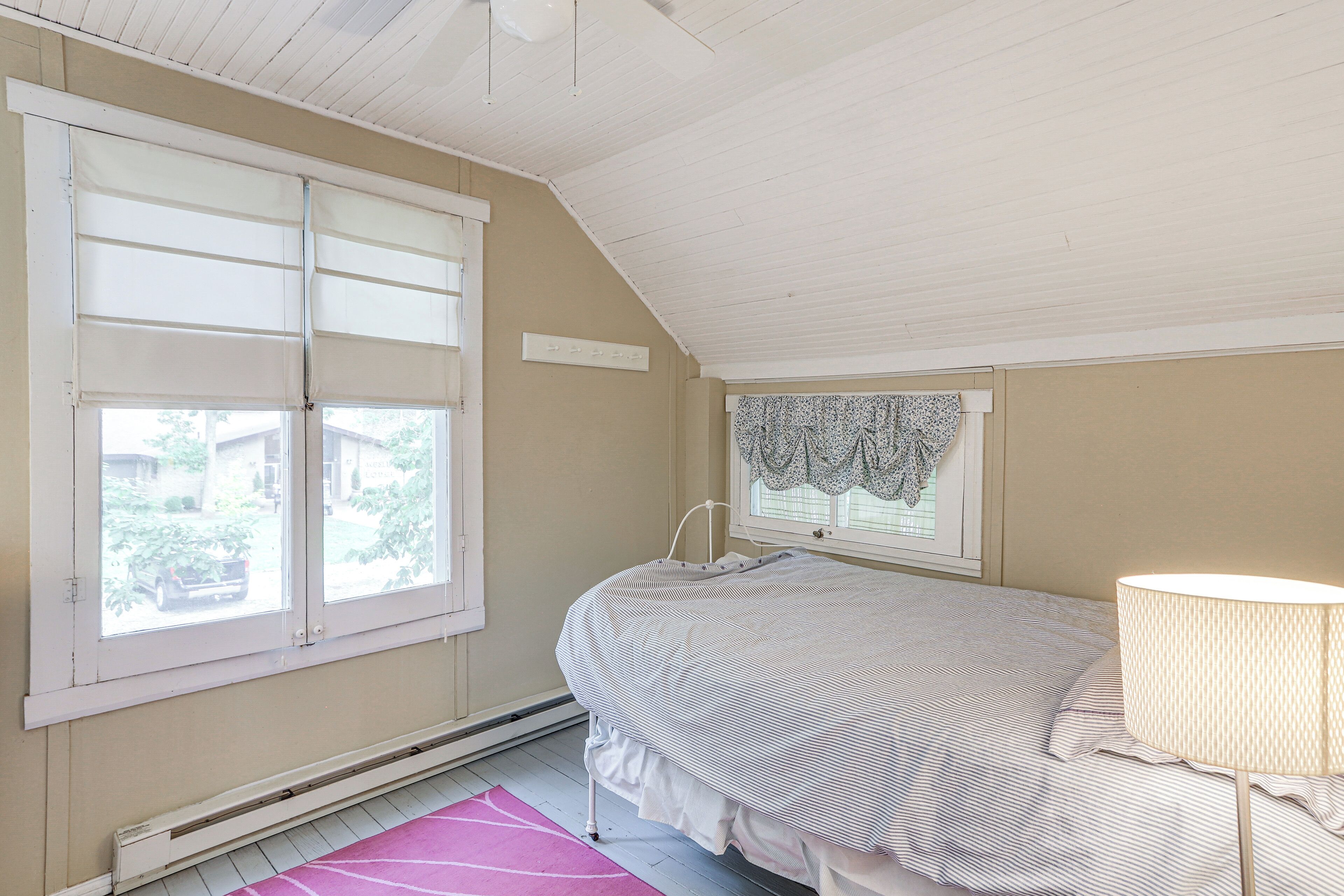 Une chambre à coucher avec un lit, une fenêtre avec des volets blancs, un radiateur et une lampe.