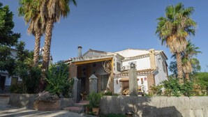 A traditional Mediterranean-style building with a tiled roof, a stone entrance, and a courtyard with palm trees.
