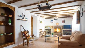 A cozy living room with exposed wooden beams, a fireplace, a sofa, and a guitar leaning against a wall.