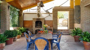 An outdoor patio with a brick fireplace, blue plastic chairs, and potted plants.