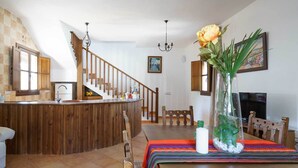 A spacious living area with a wooden staircase, a dining table with a colorful table runner, and a vase with a yellow flower.