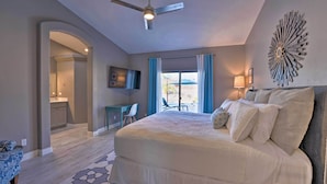 Een slaapkamer met een groot bed, een plafondventilator, een decoratieve wanddecoratie en uitzicht op het buiten.