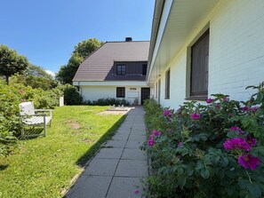 Ein Haus mit einem Weg zum Eingang, umgeben von Pflanzen und einer Bank.
