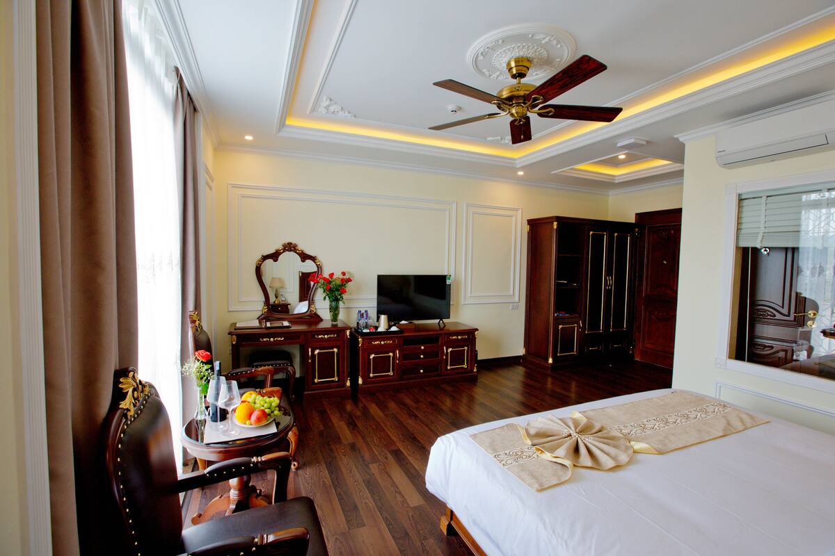 A hotel room with a bed, a desk with a computer, a television, and a dining area with a table and chairs.