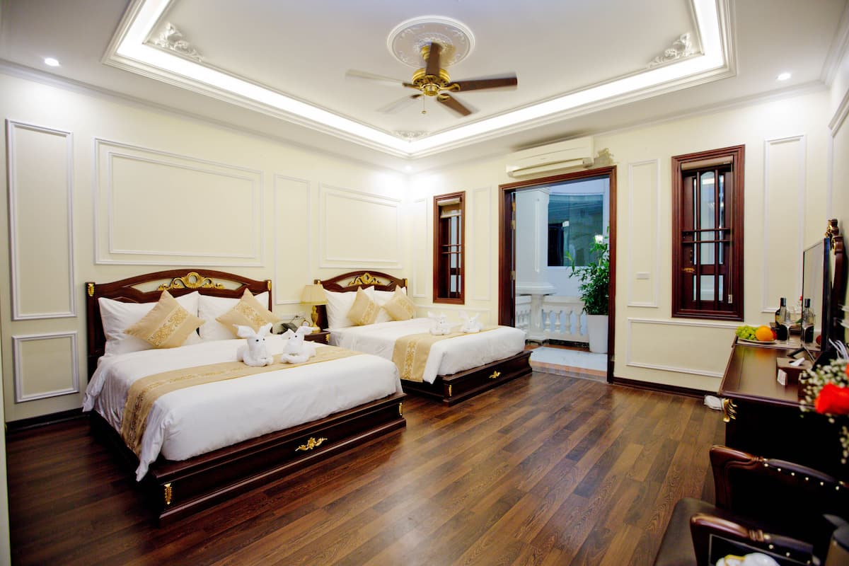 A hotel room with two beds, wooden flooring, a ceiling fan, and a balcony with a view.