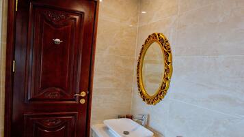A bathroom with a wooden door, a pedestal sink, a toilet, and a wall-mounted mirror.