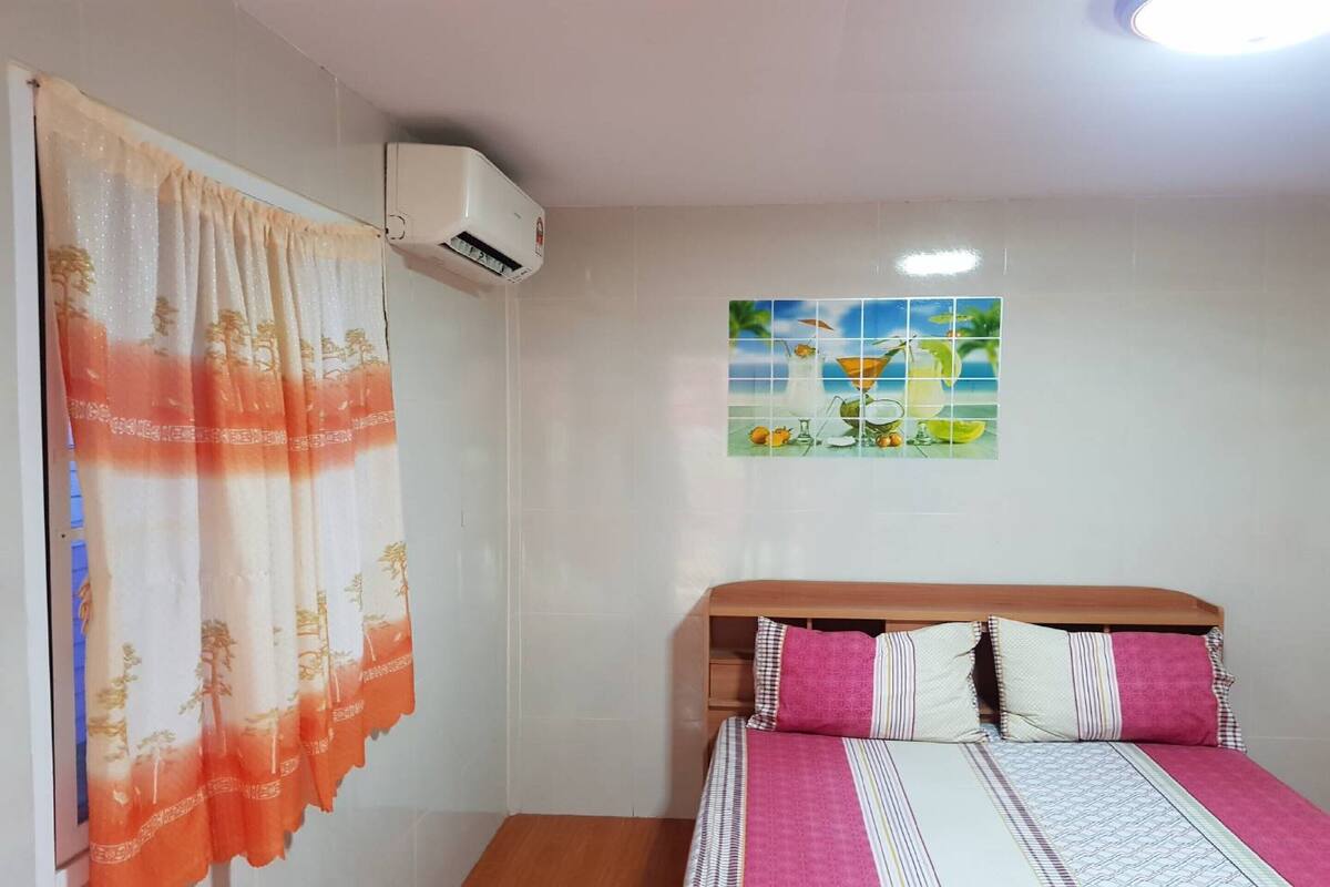 A bedroom with a bed, a wooden headboard, a wall-mounted air conditioner, and a decorative wall tile.