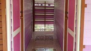 A hallway with pink walls and wooden doors, leading to a covered outdoor area. - OYO 75352 Hotel Family House And Resort Phetchaburi (Tha Yang)