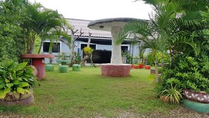 A garden with a mushroom-shaped structure, potted plants, and a building with a tiled roof in the background. - OYO 75352 Hotel Family House And Resort Phetchaburi (Tha Yang)