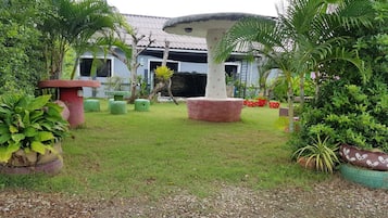 A garden with a mushroom-shaped structure, potted plants, and a building with a tiled roof in the background.