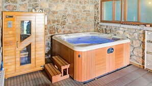 Een kamer met stenen muren, een houten sauna, een jacuzzi en een raam met gezandstraald glas.
