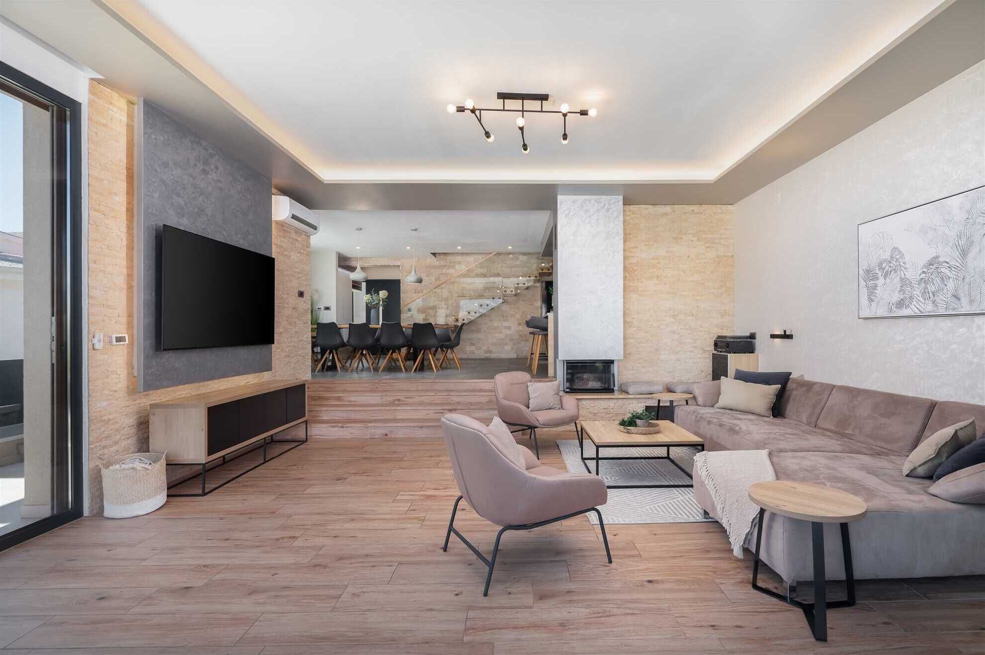 A modern living room with a flat-screen TV, a sofa, a coffee table, and a dining area with chairs.