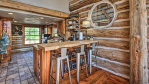 A rustic kitchen with a wooden bar and stools, a 'Gather Together' sign, and a large window. - ‘Snow Pine Retreat’ - Remote Crescent Log Cabin! (Crescent)